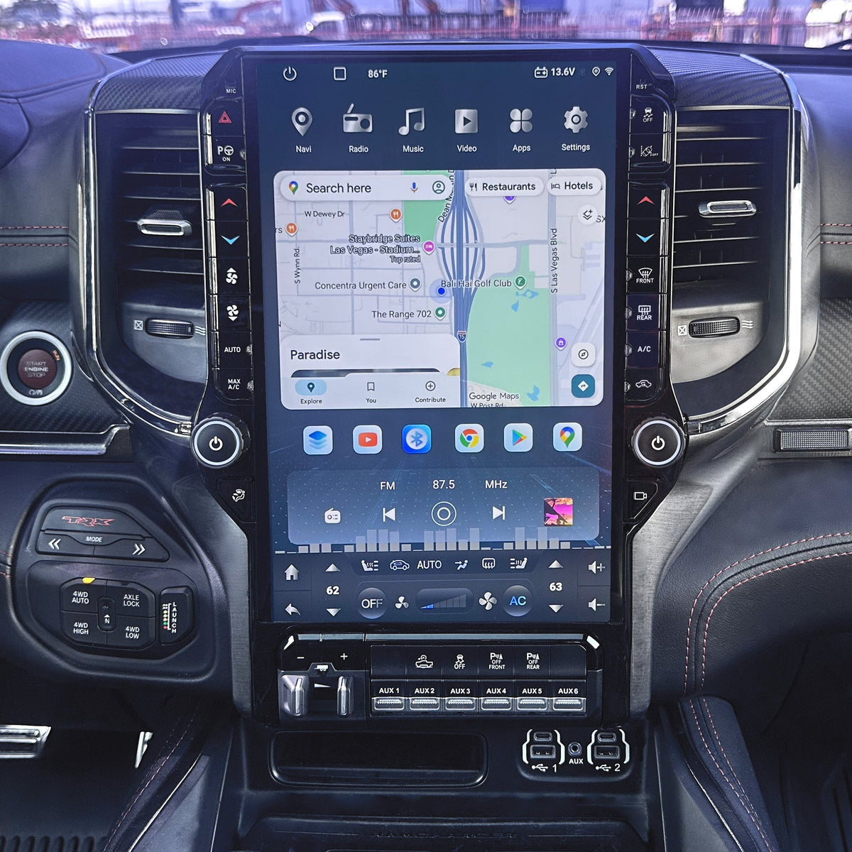A large vertical touchscreen infotainment display mounted in the center of a car dashboard, showing a map and media controls. The surrounding cabin includes air vents, climate controls, and textured trim.