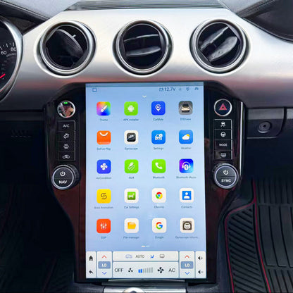 A large vertical touchscreen car infotainment display mounted in the center console, showing a colorful home screen with app icons. The dashboard around it is silver and black, with circular air vents and car interior controls visible.