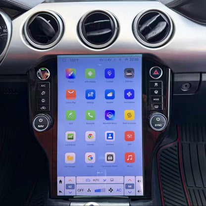 A large vertical touchscreen infotainment display mounted in the center console of a car interior, showing colorful app icons. The dashboard around it is silver and black, with circular air vents and car console controls visible.