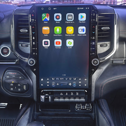 A large vertical touchscreen infotainment display mounted in the center console of a vehicle interior, showing app icons and climate controls. The dashboard, air vents, and center console are visible around it.